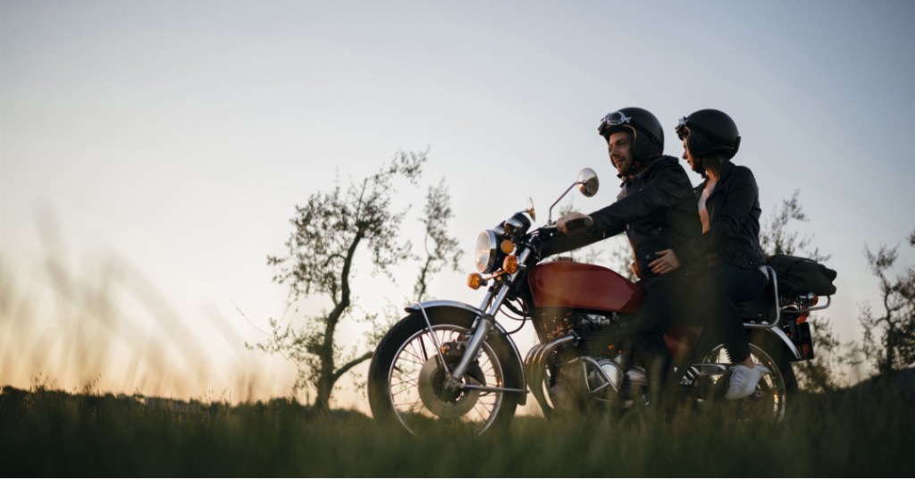Una pareja en una motora transitando por un camino rural. llevan vestidos con chaqueta y casco protector.